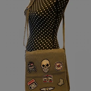 Grå axelväska med patchar - Cool grå/grön axelväska med flera broderade patchar på framsidan, Väskan har en lång axelrem som är omställbar och är i bra skick. Nästan helt oanvänd. Köpte på marknad men fick en ny väska precis efter och de slutade me att den aldrig blev andvänd. Den har ett innerfack och man får plats med det mesta. 