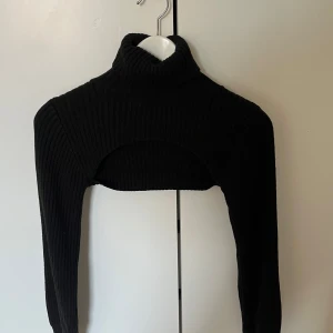 Svart ribbad croppad polotröja - Säljer en svart ribbad croppad polotröja med lång ärm och hög krage. Perfekt att styla över linnen eller klänningar för en trendig lager-på-lager-look. Supersnygg och passar till mycket!