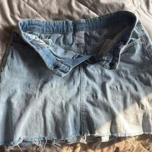 Ljusblå jeanskjol med fransig kant - Ljusblå jeanskjol från H&M  till barn storlek 134-140 (8-10) år. med klassisk femficksdesign och fransig, rå nederkant. Kjolen har bälteshällor, knapp och dragkedja framtill samt bakfickor. Liten gul fläck syns inte om man inte vet 