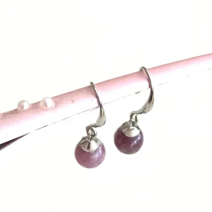 Retro/ vintage örhängen i silver med chariot-stenar - De här retro/ vintage örhängena är i sterling silver 925 och dessutom smyckade med lila charoit- stenar. Stenen charoit kommer från Sibirien, Ryssland, och är sällsynt. Den upptäcktes 1940 men blev populär runt 1970. Den har inte upptäckts på andra platser så man vet definitivt dess ursprung. Den finns i 3 olika nyanser, violett, brun och lila och detta är den lila sorten.Man kan luras att tro att det är en sorts pärla pga hur den känns men det är alltså en kristall som används i kristallterapi 