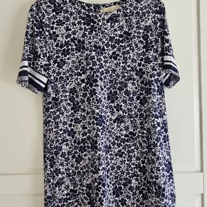 Blommig blåvit klänning Michael Kors  - Säljer en blåvit klänning med blommigt mönster. Klänningen har korta ärmar och är tillverkad i ett mjukt material, perfekt för en avslappnad stil. Stretchig skrynklar inte m/l