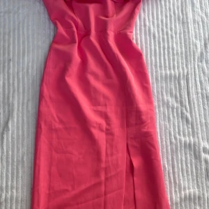 Rosa långklänning med volang - Snygg rosa långklänning från Miss Selfridge med axelbandslös look och bred volang upptill. Klänningen har smala axelband och figurnära passform som ger en elegant siluett. Perfekt för dig som vill sticka ut med färg och stil.