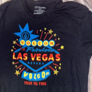 Svart Volcom Las Vegas t-shirt - Svart t-shirt från Volcom med färgglatt Las Vegas-tryck i blått, gult och rött framtill. Klassisk passform och rund hals. Tillverkad i 100% bomull, perfekt för dig som gillar streetwear och grafiska prints. Köpt i USA