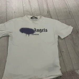 Vit Palm Angels t-shirt London print - Vit t-shirt från Palm Angels med klassiskt svart London-tryck på bröstet och lila spray paint-detalj över loggan. T-shirten har rund hals, korta ärmar och är gjord i mjuk bomull. Använd fåtal gånger. Pris kan diskuteras!