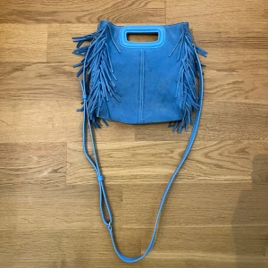 Blå väska i suede leather från Maje - Säljer min blåa axelväska från Maje. Väskan har en justerbar axelrem som även går att ta bort. Väskan har lite skavanker, fransarna högst upp på väskan är mörkare än resterande. 23x20 cm. Kvitto finns.