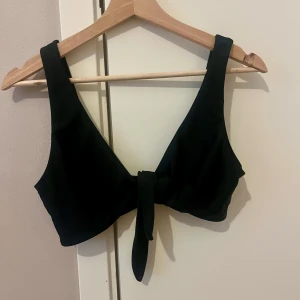 Svart bikiniöverdel - Snygg svart bikiniöverdel med breda axelband och knyt framtill från Nelly.