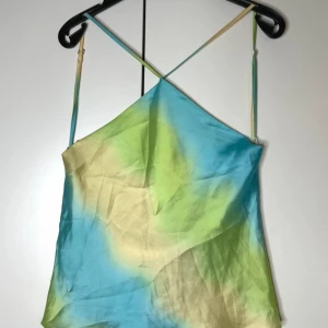 Färgglad haltertopp med smala axelband - Säljer min snygga haltertopp med tunna axelband och korsad rygg. Toppen är tyvärr för liten, älskar att har ett unikt mönster i blått, grönt och beige med en lätt glansig finish. Perfekt för varma dagar och somriga outfits.