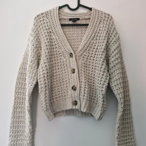 Beige stickad kofta från Esmara - Säljer en beige stickad kofta från Esmara med grovstickat mönster och stora knappar framtill. Koftan är croppad och har långa ärmar samt bred ribbad mudd vid ärmslut och nederkant. Perfekt för lager-på-lager-stil! Tråddragningar finns och längst ner längsknappraden har en tråd gått av.