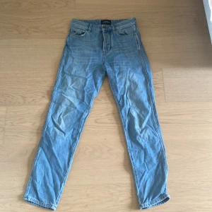 Blå jeansbyxor från J.Lindeberg - Snygga blå jeans från J.Lindeberg med klassisk femficksdesign och silverfärgade detaljer. Byxorna har normal passform och raka ben. Perfekta för en stilren och avslappnad look. Jag vet inte den exakta storleken för jag hittade den inte men gissar på att byxorna har storlek 152-158. Det går självklart super att pröva jeansen på plats!🥰