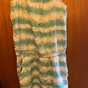 Blåvit ärmlös jumpsuit från H&M - Säljer en ärmlös jumpsuit i blått och vitt med batikmönster. Jumpsuit har resår i midjan, fickor och en snygg knytning samt öppning i ryggen. Perfekt för varma dagar! (Barn)