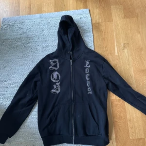 Rhinestone hoodie - Svart hoodie med dragkedja och huva, dekorerad med stora strasstenar i mönster och text på både fram- och baksidan. Tröjan har känguruficka och långa ärmar. Perfekt för dig som gillar streetstyle och vill sticka ut.
