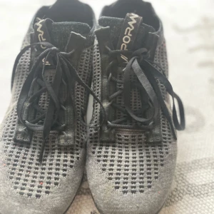 Nike Vapormax svarta sneakers - Nike Vapormax sneakers i svart med stickad ovandel och vita detaljer. Skorna har snörning, synlig logga på plösen och en unik genomskinlig sula. Perfekta för dig som gillar sportig stil och vill ha något bekvämt och luftigt på fötterna.