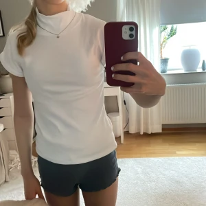 Vit t-shirt med hög krage - Säljer en stilren vit t-shirt med hög krage och korta ärmar. T-shirten har en clean look och är perfekt för dig som gillar minimalistisk stil. Materialet känns mjukt och bekvämt mot huden. Passar till allt och är enkel att matcha.