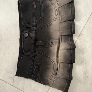 Svart jeanskjol med hjärtfickor - Superfin svart jeanskjol med cool tvättad effekt och plisserad nederkant. Kjolen har två knappar framtill, bälteshällor och bakfickor med hjärtformad söm. HELT oanvänd!!