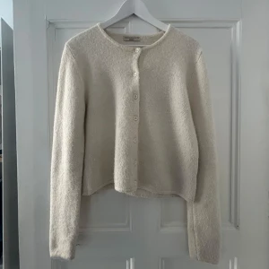 Beige kofta från Gina Tricot - Vit kofta från Gina Tricot med rund halsringning och knäppning framtill. Lite nopprig men inget som förstör utseendet. Storlek M