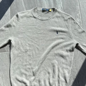 Ralph Lauren Sweatshirt - Snygg grå stickad tröja från Polo Ralph Lauren med klassisk rund halsringning och broderad marinblå logga på bröstet. Går att få den lägre vid snabb affär