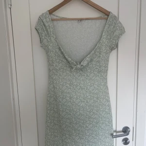 Ljusgrön blommig klänning Nelly - Supersöt ljusgrön kortklänning från Nelly med små vita blommor, v-ringning och knyt fram.