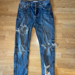 Blå slitna jeans från ZARA - Säljer ett par blå jeans från ZARA med rejält slitna detaljer och hål på benen. Jeansen har klassisk femficksdesign, normal passform och raka ben. Perfekta för en avslappnad och trendig look.