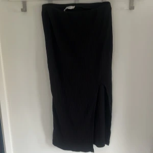 Svart ribbad långkjol från ONLY - Svart ribbad långkjol från ONLY med en snygg slits framtill. Kjolen är i stretchigt material och har en enkel, stilren design som passar till många olika looks.