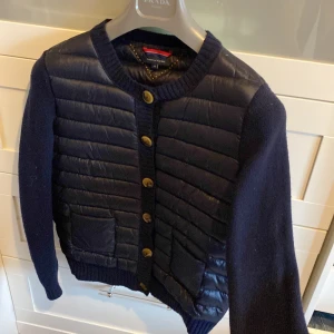 Tommy Hilfiger quiltad cardigan - Snygg och trendig quiltad cardigan/jackan från Tommy Hilfiger med stickade ärmar och quiltad fram och baksida. Även två fickor på framsidan och stängning med knappar. Fin marinblå färg och perfekt för höst och vår! Liknar de populära Moncler cardigansen   Fint skick, en liten defekt är dock att sista knappen saknar en liten del, men är inget som man tänker så mycket på och den går fortfarande att stänga som vanligt. 
