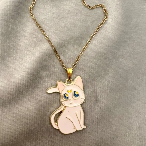 Artemis Halsband Sailor Moon - Ett gulligt halsband med katten Artemis från Sailor Moon 🌙 💕 Kedjan är i guldimitation och justerbar 40-45 cm. Berlocken är ca 3 x 2 cm. Perfekt present för ett Sailor Moon-fan!