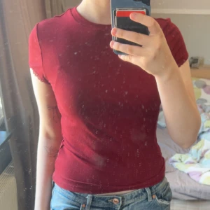 Röd ribbad croppad t-shirt - Säljer en tight röd ribbad t-shirt med korta ärmar och croppad passform. Ärmsluten har en liten spetskant som ger en söt detalj. Perfekt till jeans eller kjol. Använd enstaka gång.