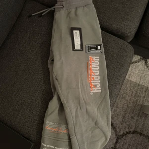 Gråa mjukisbyxor från Hoodrich - Säljer ett par gråa mjukisbyxor från Hoodrich med tryckt logga i vitt och orange på benet. Byxorna har dragsko i midjan och muddar vid bensluten. Perfekta för en avslappnad stil. Ett år gammal köpt från JD för 800kr och säljer nu för 300kr