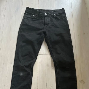Svarta jeans från Nudie Jeans - Säljer ett par svarta jeans från Nudie Jeans med klassisk femficksdesign och silverfärgade nitar. Jeansen har använts ett par gånger och har en vit markering på högra knäet vilket knappt syns när man väl har på sig dem. Jeansen har en klassisk slim passform. Perfekta för dig som gillar stilrena och tidlösa byxor. Priset är inte hugget i sten. Om du har några frågor eller vill ha lite fler bilder så är det bara att höra av dig. 