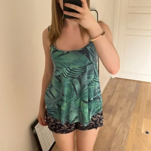 Grön mönstrad linnetopp från Gina Tricot - Säljer en snygg linnetopp från Gina Tricot i storlek XS. Toppen har smala axelband och ett tropiskt blad-mönster i olika gröna nyanser. Perfekt för varma dagar och enkel att matcha med shorts eller kjol. Säljer eftersom jag inte använder det längre, bara använd två gånger! Köpt för runt 200kr. Kontakta för mer information! 💖