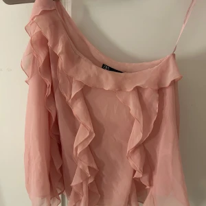 Rosa volangblus från Zara - Säljer en superfin rosa blus från Zara med volangdetaljer och en axelbandslös design. Storlek L men den passar mig bra som vanligtvis har S/M💗