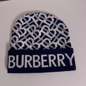 Mönstrad mössa från Burberry - Snygg mössa från Burberry i blått och vitt med grafiskt mönster och stor logga framtill. Stickad i mjukt material och har uppvikt kant. Perfekt för att hålla värmen med stil.