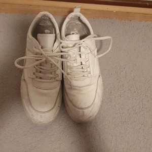 Vita sneakers med snörning - Stilrena vita sneakers med klassisk design och snörning. Skorna har rund tå, platt sula och är tillverkade i syntetmaterial. Perfekta för dig som gillar en clean och enkel look till vardags. Passar till det mesta och är lätta att matcha.