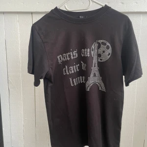 Svart t-shirt - Svart t-shirt med text ”Paris au clair de lune”. Säljer för att jag har vuxit ur den. Och den är använd npgra gånger, lappen vid nacken är borta. Därför den säljs så billigt.