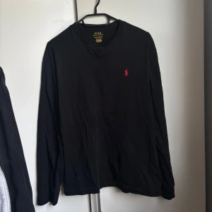 Polo Ralph Lauren tröja - Svart långärmad tröja från Polo Ralph Lauren med klassisk v-ringning och röd broderad logga på bröstet. 