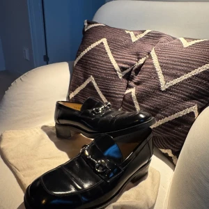 Svarta loafers från Gucci i skinn - Klassiska svarta loafers från Gucci i blankt skinn med silverfärgad hästbitsdetalj över vristen. Snygg, tidlös design med låg klack och rund tå. Perfekta för dig som vill ha en stilren och lyxig look. Nypris 11 tusen!