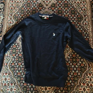 Mörkblå merino wool tröja från U.S polo assn. - Mörkblå långärmad merino wool tröja från u.s polo assn. med rund halsringning och liten broderad logotyp på bröstet. Klassisk och stilren modell i mjukt material, perfekt för en avslappnad men snygg look. Tröjan är storlek M men passar som S eftersom att den krympt i tvätten.