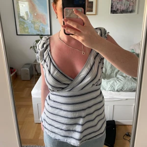 Randig omlottopp med volangärmar från H&M - Säljer en vit omlottopp med blåa ränder. Toppen har volangdetaljer på axlarna, knyt i ryggen och v-ringning framtill.
