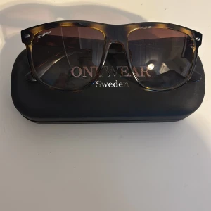 Bruna solglasögon från ONEWear - Snygga solglasögon från ONEWear med brunmelerat båge och stora, fyrkantiga glas. Kommer med originalfodral och putsduk. Perfekta för att ge en cool touch till din stil.