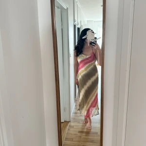 Boho-inspirerad Slipklänning i strl M - Långklänning med batikmönster i olivgrönt, beige och rosa. Klänningen har tunna axelband med pärldetalj i ryggen. Klänningen har bara använts en gång och är i storlek M, från Zara. 