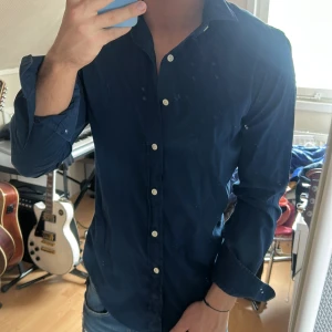 Mörkblå skjorta från Ralph Lauren - Säljer en klassisk mörkblå skjorta från Ralph Lauren med broderad logga på bröstet. Skjortan har långa ärmar, vit knappstängning och en tidlös passform som funkar till många tillfällen.