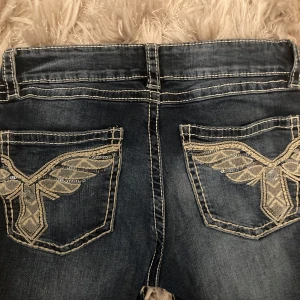 Mörkblå jeans med broderade bakfickor - Säljer ett par mörkblå jeans med snygga kontrastsömmar och broderade detaljer på bakfickorna. Jeansen har låg midja och klassisk bootcut-modell. 