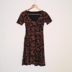 Indiska klänning strl S - Klänning från Indiska strl S svart med orange-brunt blommigt tryck. Mått: 68cm i midjan, 84 cm lång, ärmar 19,5 cm från axel, stretchig. Kan fixa fler bilder och mått vid intresse! 