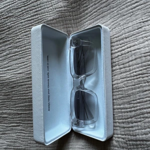 Transparenta solglasögon från CHIMI - Snygga, rektangulära solglasögon från CHIMI med transparent båge och mörka glas. Kommer i originalfodral. Perfekt accessoar för en trendig look.