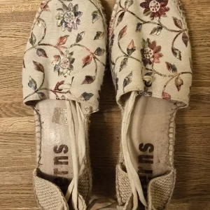 Blommiga espadrillos med platåsula - Säljer ett par espadrillos med blommigt broderi i flera färger på beige tyg. Skorna har platåsula i flätad jute och knytband runt ankeln. Perfekta för sommaren och ger en bohemisk känsla till outfiten.