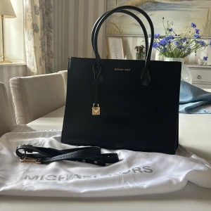 Michael Kors handväska - Säljer en helt ny, oanvänd handväska från Michael Kors med guldiga detaljer och lås. Väskan har två handtag och medföljer en axelrem. Perfekt till skolan eller jobbet. Kom gärna med prisförslag. Mått: 33x25cm