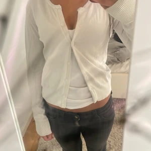 Vit kofta från H&M Basics - Säljer en klassisk vit kofta från H&M Basics i storlek XS. Koftan har långa ärmar, rund halsringning och knäppning framtill med små vita knappar. Perfekt att slänga över en topp eller klänning. Materialet känns mjukt och lätt.