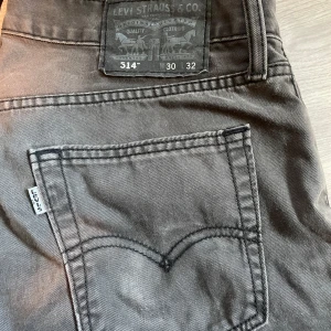 Svarta Levis 514 jeans vintage - Säljer ett par svarta Levis 514 jeans med klassisk femficksdesign och raka ben. Byxorna har Levis-logga på bakfickan och patch bak i midjan. Perfekta för dig som gillar en tidlös och stilren look.