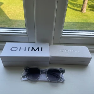 Grå transparenta solglasögon från CHIMI - Säljer ett par stilrena solglasögon från CHIMI med transparent grå båge och mörka glas. Kommer med originalförpackning och fodral. Perfekta för dig som vill ha en modern och clean look. Väldigt bra skick, använda fåtal gånger. Perfekt inför sommaren när solen är framme. Pris kan diskuteras vid snabb affär. 