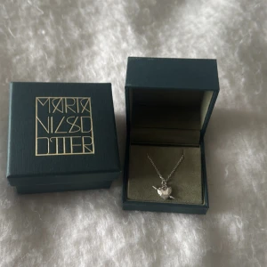 Silverhalsband med fågelhjärta från Maria Nilsdotter - Säljer nu mitt Maria Nilsdotter halsband pga att den inte kommer till användning längre. Den är köpt för 2800kr i Maria nilsdotters butik i Stockholm. Boxarna följer med om halsbandet köps. Längden på halsbandet är 40cm. För mer frågor eller bild skriv privat☺️ Säljer för 1600kr men priset kan diskuteras 