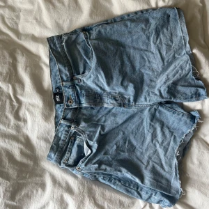 Ljusblå jeansshorts från 157 - Säljer ett par ljusblå jeansshorts från 157 i storlek L. Klassisk femficksmodell med råa, fransiga benslut och hög midja. Perfekta för varma dagar och enkel att matcha med olika toppar.